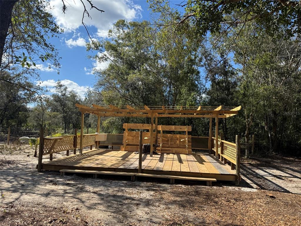 A wooden deck with a pergola and built-in seating stands in a wooded area — 17618 NW 286TH STREET, OKEECHOBEE, FL