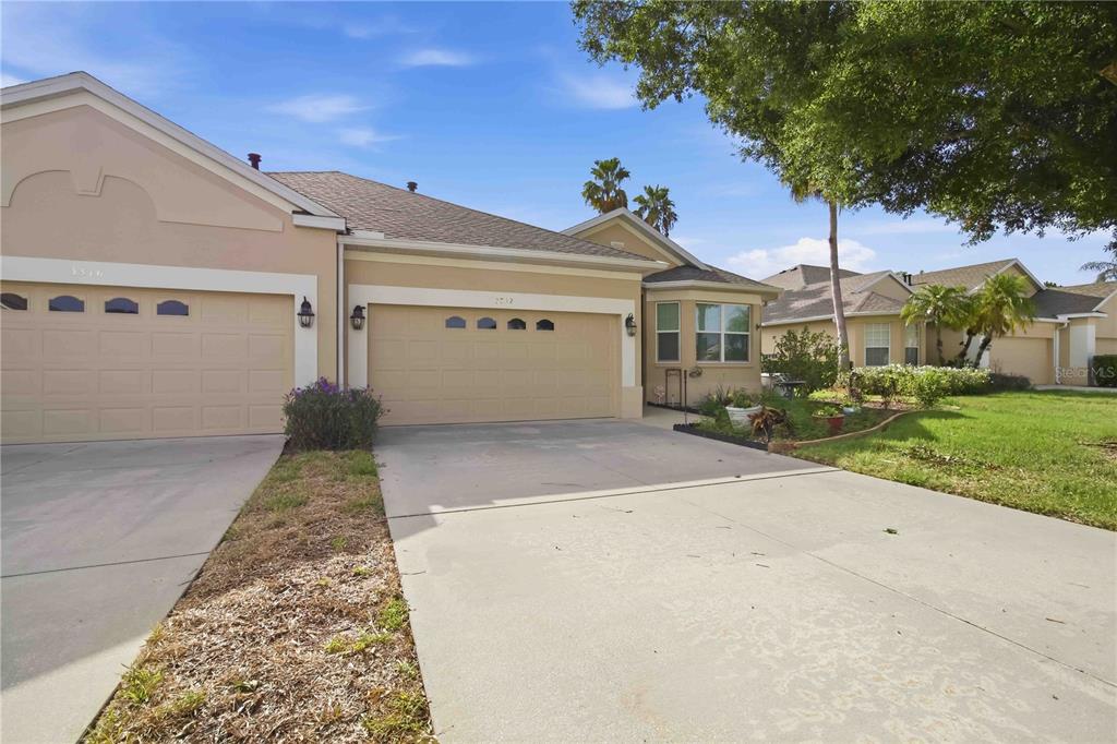A tan suburban house features a two-car garage, a concrete driveway, and a landscaped yard — 3312 92ND AVENUE E, PARRISH, FL