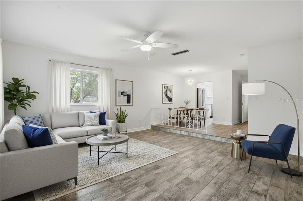 A living room with light wood-look tile floors, a gray sectional, and a raised dining area — 6927 PLACE DE LA PAIX UNIT 6927, ST PETERSBURG, FL