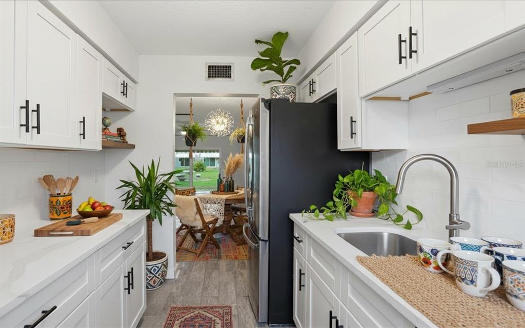 A galley kitchen features white cabinets, black hardware, a stainless steel refrigerator, and a sink — 6927 PLACE DE LA PAIX UNIT 6927, ST PETERSBURG, FL