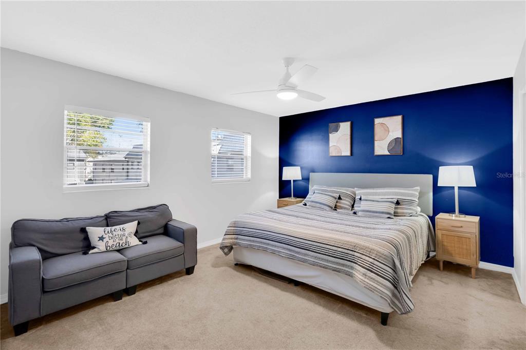 A bedroom features a bed against a dark blue wall, a grey sofa, and carpet — 6927 PLACE DE LA PAIX UNIT 6927, ST PETERSBURG, FL