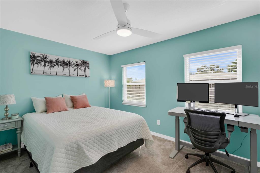 A bedroom features light blue walls, a bed with pink pillows, and a dual-monitor desk — 6927 PLACE DE LA PAIX UNIT 6927, ST PETERSBURG, FL