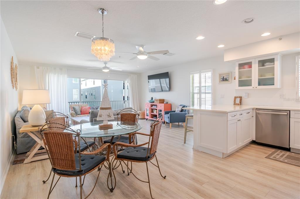 An open-concept living and dining area features light wood floors, white cabinetry, and wicker chairs — 1904 GULF BOULEVARD UNIT D, INDIAN ROCKS BEACH, FL