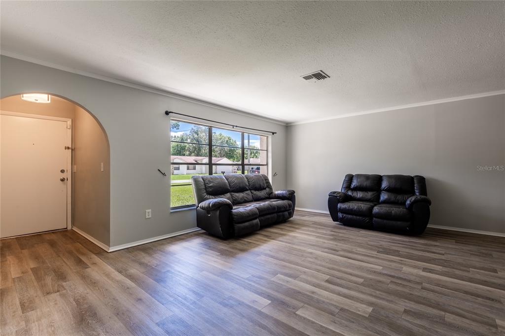A living room with light gray walls, wood-look flooring, two black leather sofas, and an archway — 1257 FINLAND DRIVE, SPRING HILL, FL