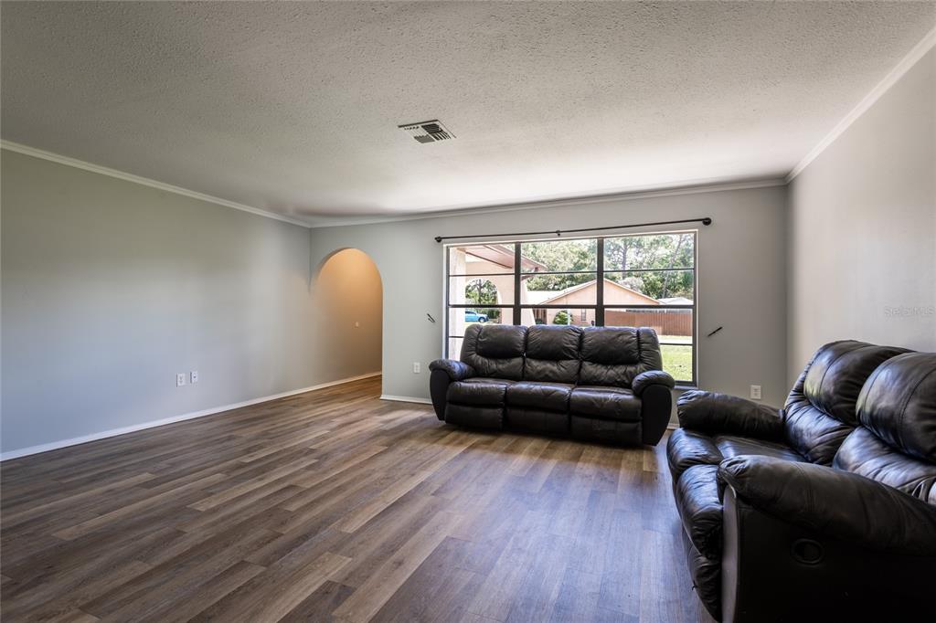 A living room features light gray walls, wood-look flooring, two black leather sofas, and a large window — 1257 FINLAND DRIVE, SPRING HILL, FL