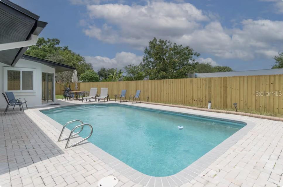 A rectangular swimming pool sits on a paved patio next to a house and fence — 8622 BAYLOR CIRCLE, ORLANDO, FL