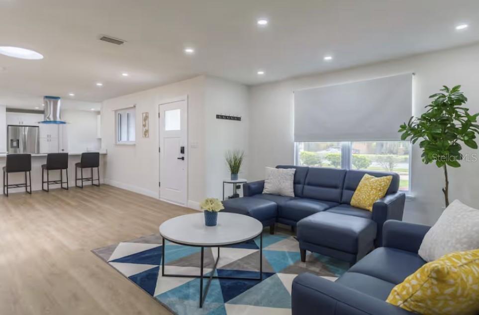 A living room with blue sectional sofas, a geometric rug, and an open kitchen area — 8622 BAYLOR CIRCLE, ORLANDO, FL