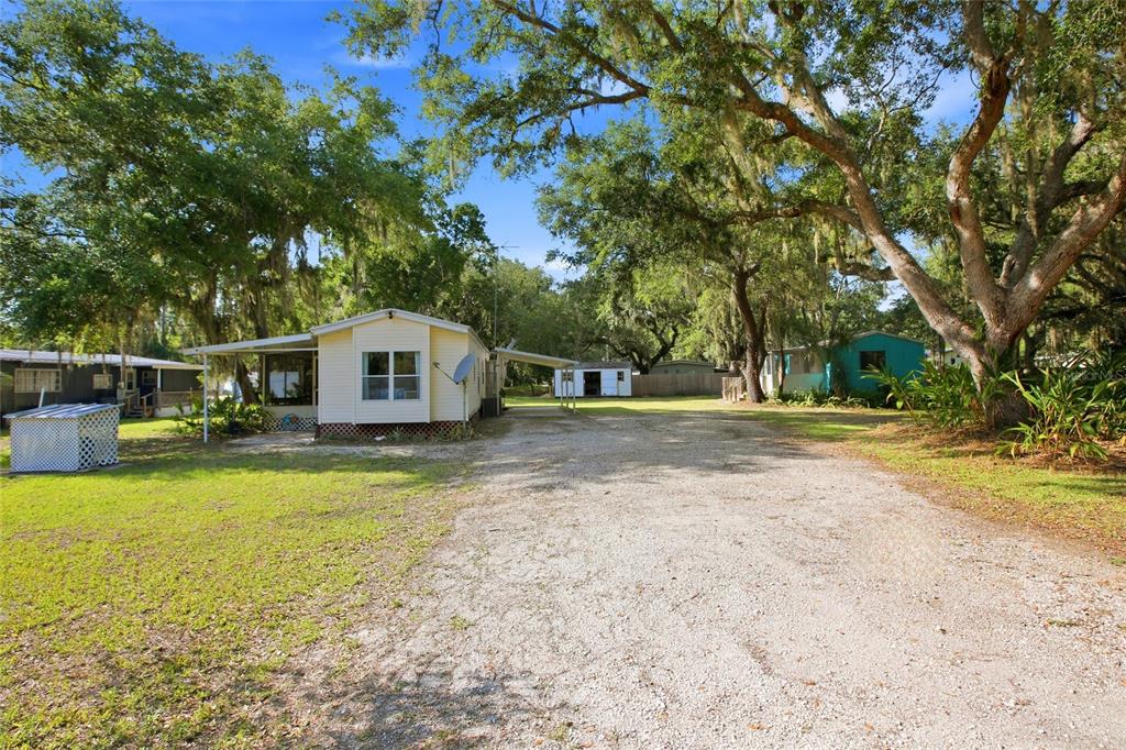 A blue mobile home features a wooden deck and a screened-in porch under large trees — 3348 OMEC STREET, LAKE WALES, FL