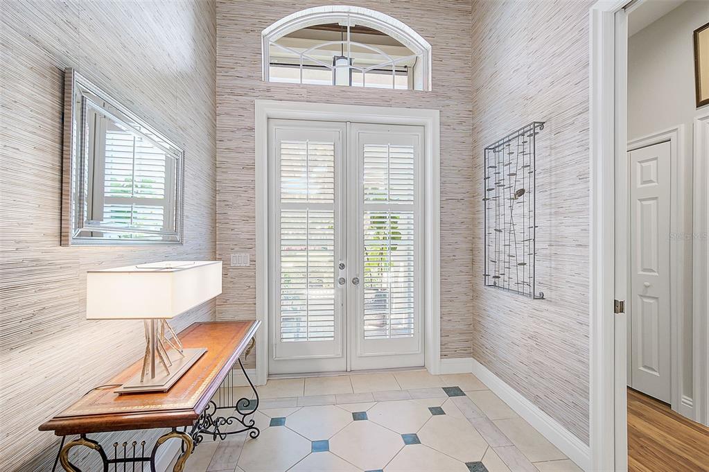 A foyer features textured wallpaper, a wooden console table, and double doors with plantation shutters — 293 TURQUOISE LANE, OSPREY, FL