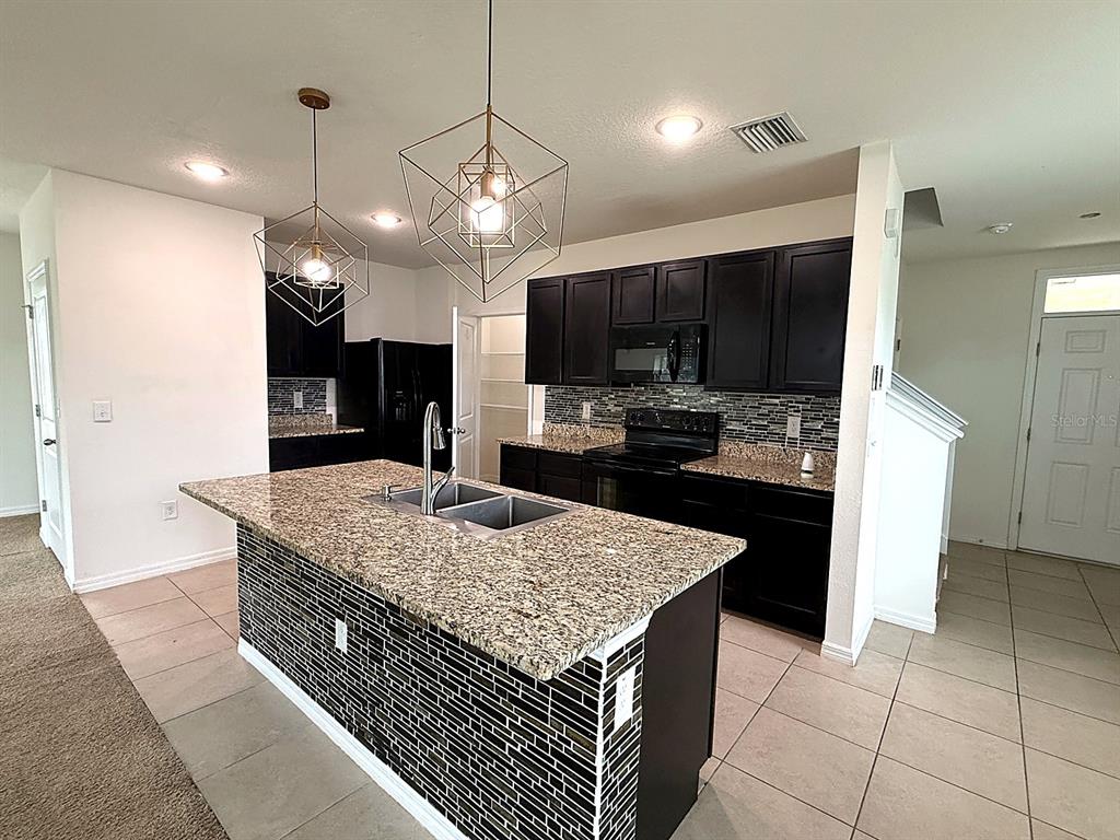 A kitchen features dark cabinets, granite countertops, a tiled island, and a stainless steel faucet — 32649 PEZ LANDING LANE, WESLEY CHAPEL, FL