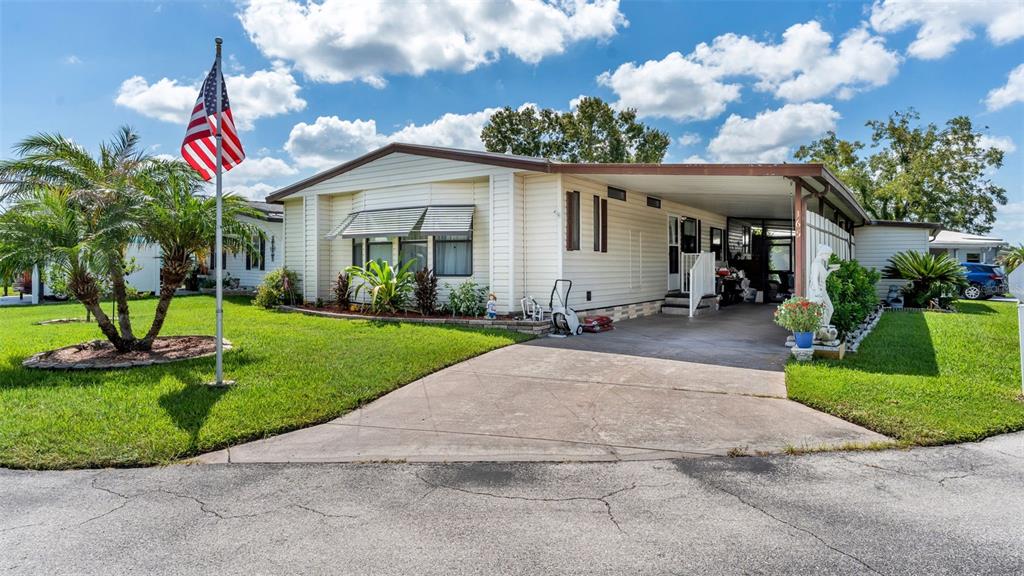 A single-story manufactured home features a concrete driveway, a carport, and an American flag — 2055 S FLORAL AVENUE UNIT 165, BARTOW, FL