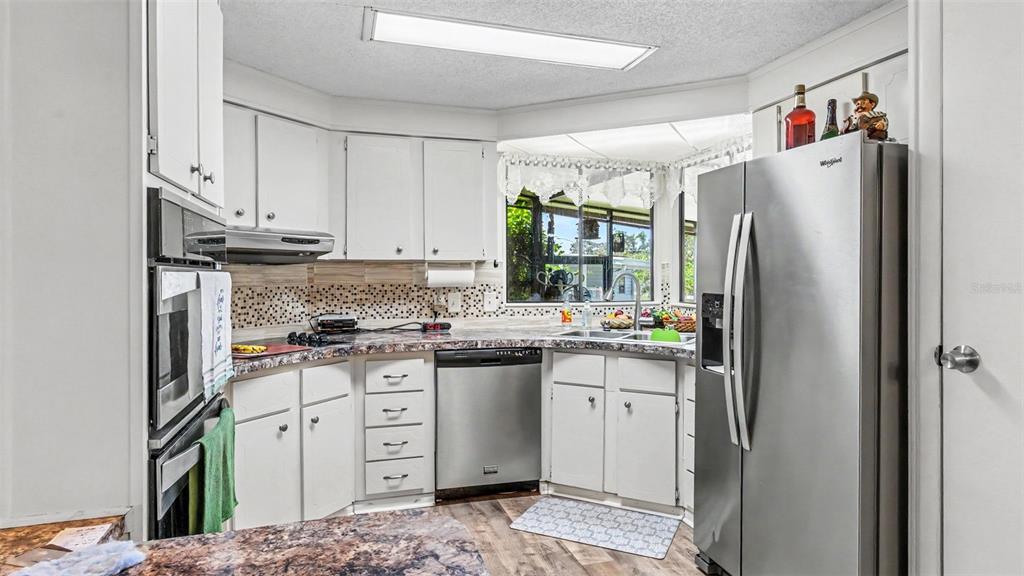 A kitchen features white cabinets, stainless steel appliances, a patterned backsplash, and wood-look flooring — 2055 S FLORAL AVENUE UNIT 165, BARTOW, FL