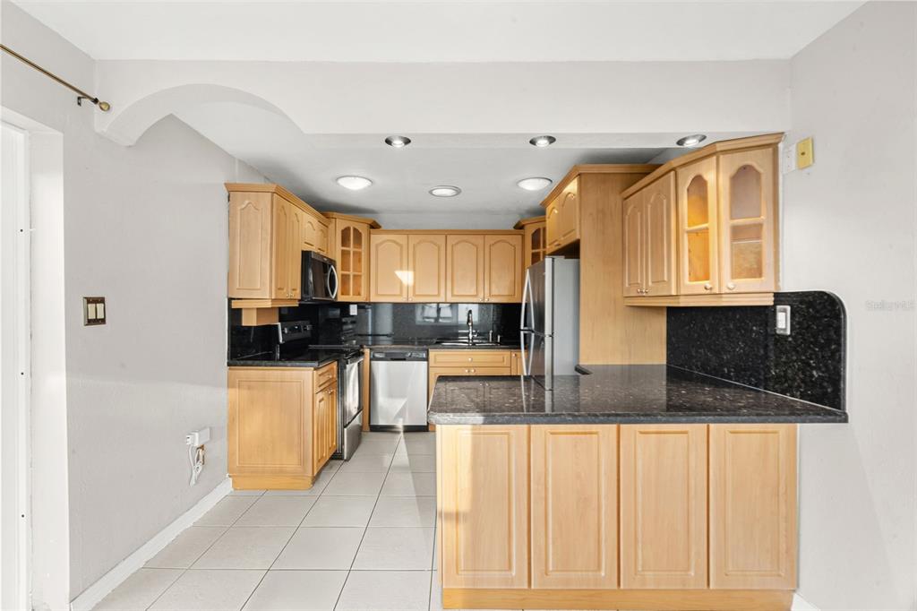 A kitchen with light wood cabinets, black countertops, stainless steel appliances, and beige tile flooring — 2913 MCINTOSH ROAD, SARASOTA, FL