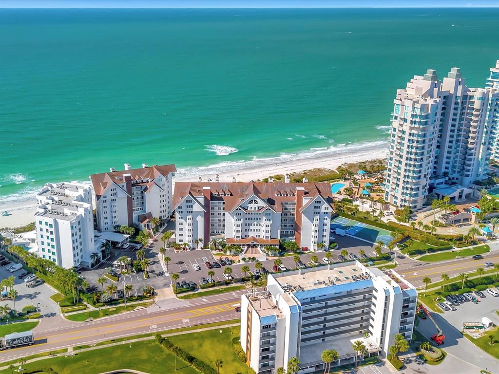An aerial view shows several large beachfront apartment buildings along a sandy coastline — 1582 GULF BOULEVARD UNIT 1203, CLEARWATER, FL