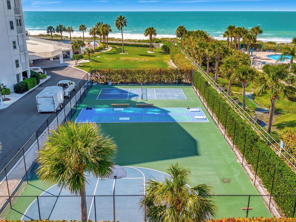 An aerial view shows a basketball court and pickleball courts next to a beachside building — 1582 GULF BOULEVARD UNIT 1203, CLEARWATER, FL