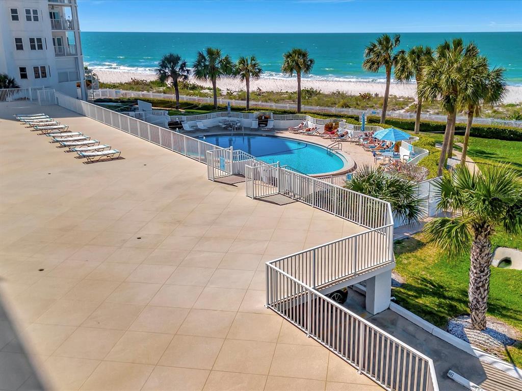 An elevated view of a swimming pool and patio area overlooking a sandy beach and ocean — 1582 GULF BOULEVARD UNIT 1203, CLEARWATER, FL