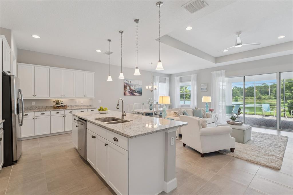 A bright open-concept kitchen and living area with white cabinets, granite countertops, and lake views — 1649 VICTORIA GARDENS DRIVE, DELAND, FL