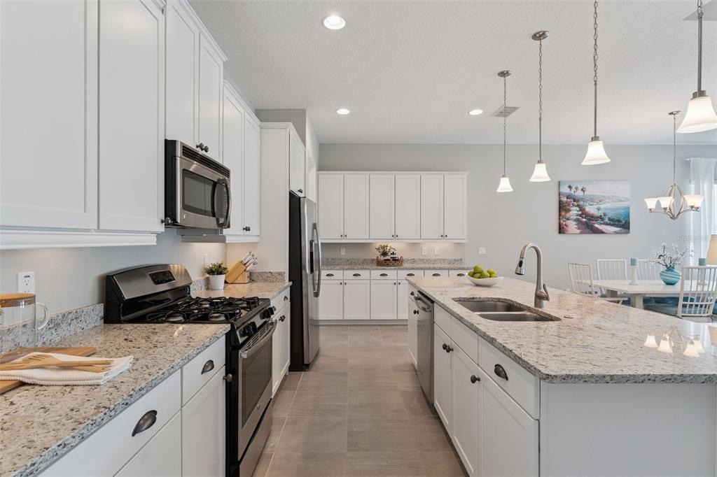A modern kitchen features white cabinets, granite countertops, stainless steel appliances, and a central island — 1649 VICTORIA GARDENS DRIVE, DELAND, FL
