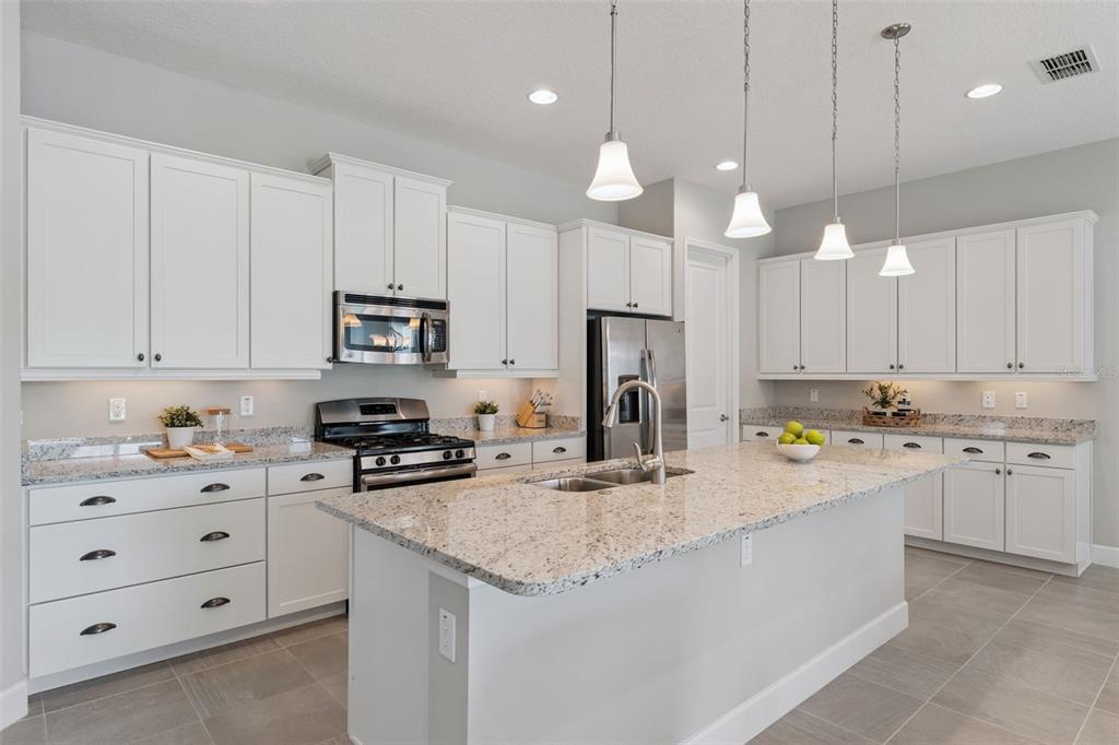 A modern kitchen features white cabinetry, granite countertops, a central island, and stainless steel appliances — 1649 VICTORIA GARDENS DRIVE, DELAND, FL