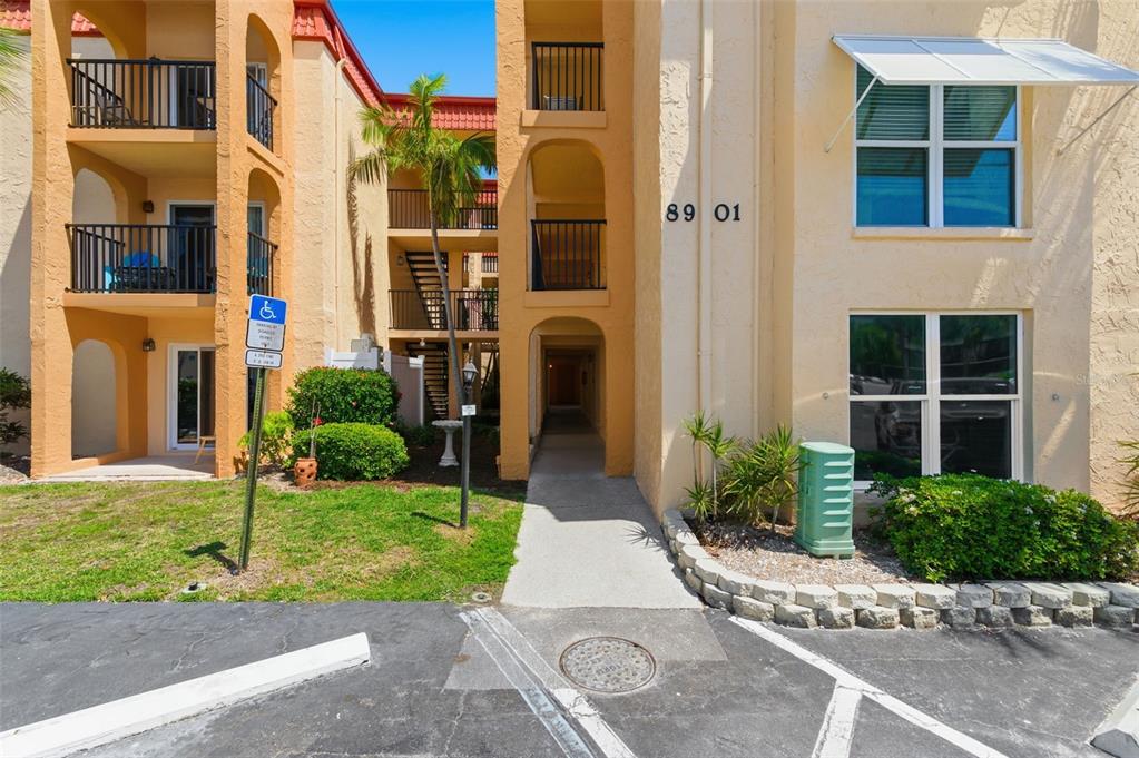 The exterior of a multi-story apartment building features a walkway leading to a central entrance — 8901 BLIND PASS ROAD UNIT 124, ST PETE BEACH, FL