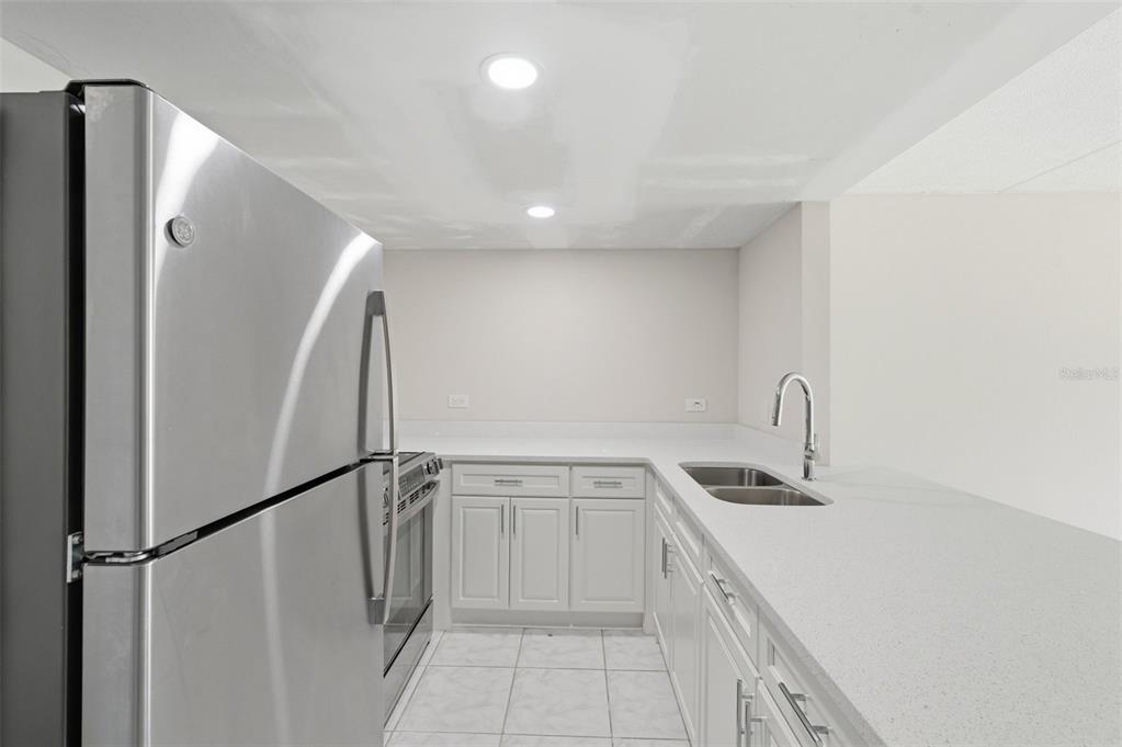 A kitchen features white cabinets, light countertops, stainless steel appliances, and tile flooring — 8901 BLIND PASS ROAD UNIT 124, ST PETE BEACH, FL