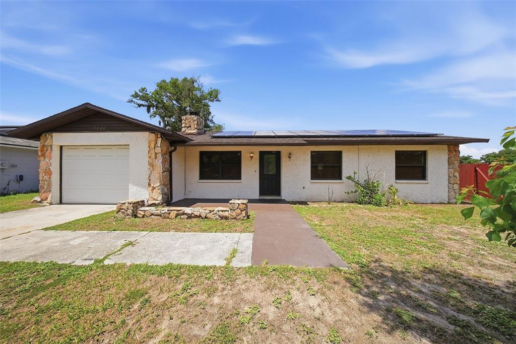 A single-story house with a white stucco exterior, stone accents, and solar panels on the roof — 5020 PINE STREET, SEFFNER, FL