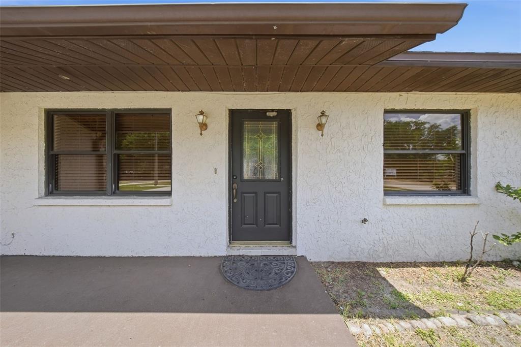 A front exterior view of a house with a dark door, two windows, and stucco walls — 5020 PINE STREET, SEFFNER, FL