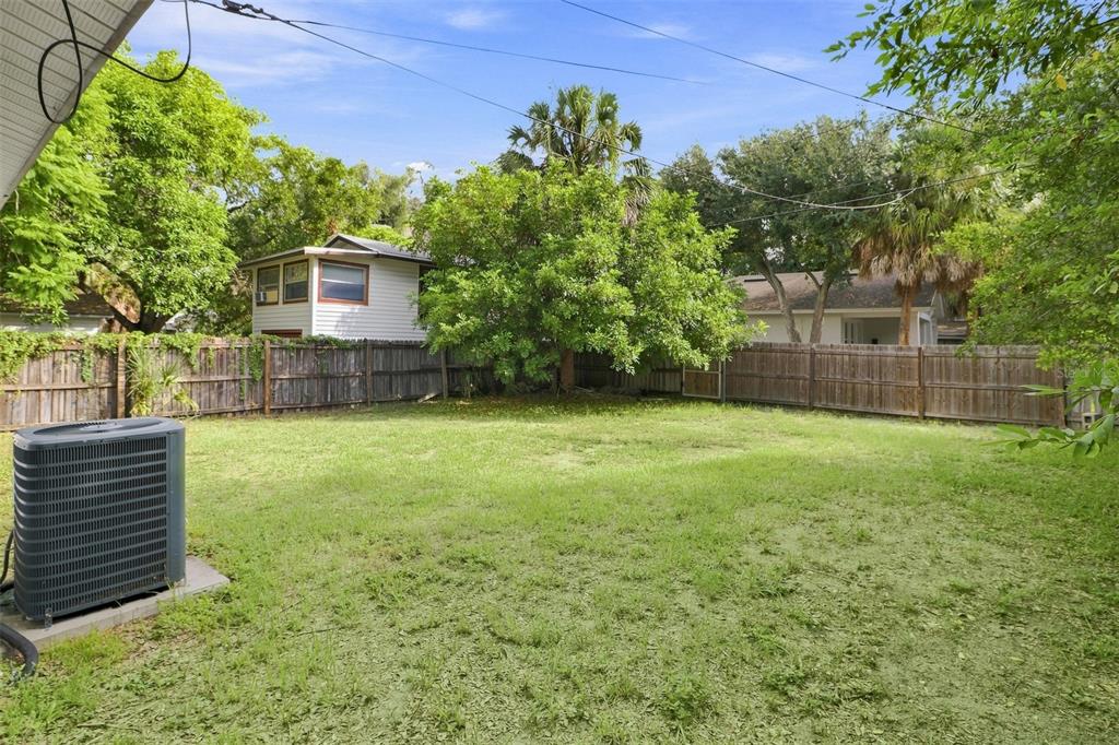 A grassy backyard features a wooden fence, a large tree, and an outdoor air conditioning unit — 2324 OAKDALE STREET S, ST PETERSBURG, FL