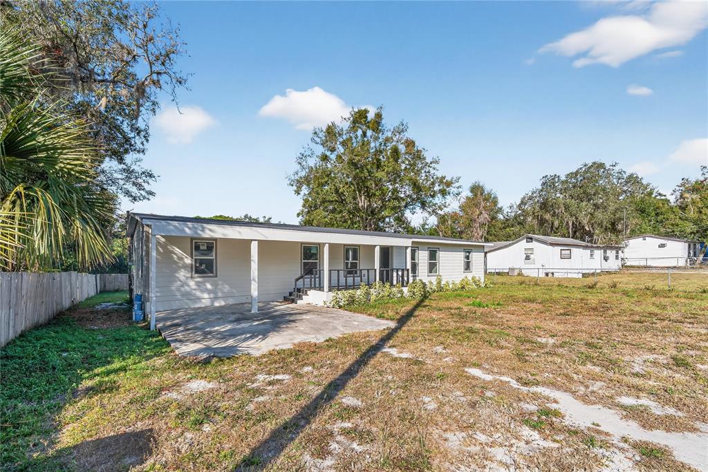 A single-story manufactured home features a covered patio and a large, grassy yard — 40415 COUNTRY ROAD, EUSTIS, FL