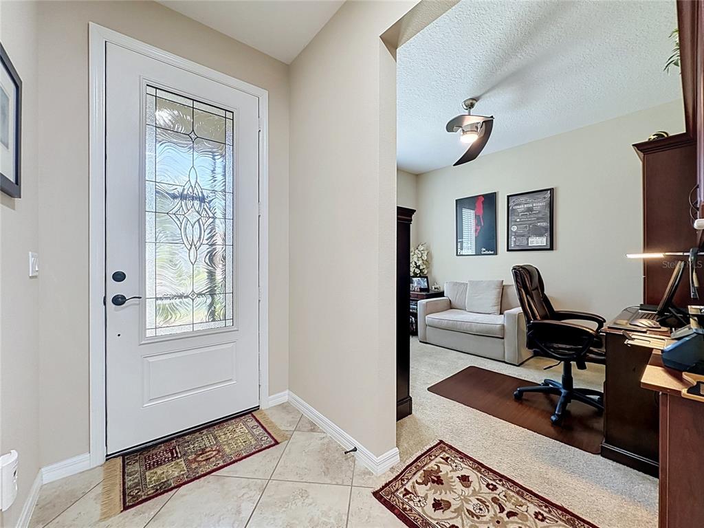 A tiled entryway leads into a carpeted home office featuring a desk and sofa — 164 SILVER MAPLE ROAD, GROVELAND, FL