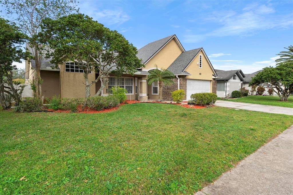 A tan suburban house with a two-car garage, a front lawn, and mature trees — 12512 TILLINGHAM COURT, ORLANDO, FL