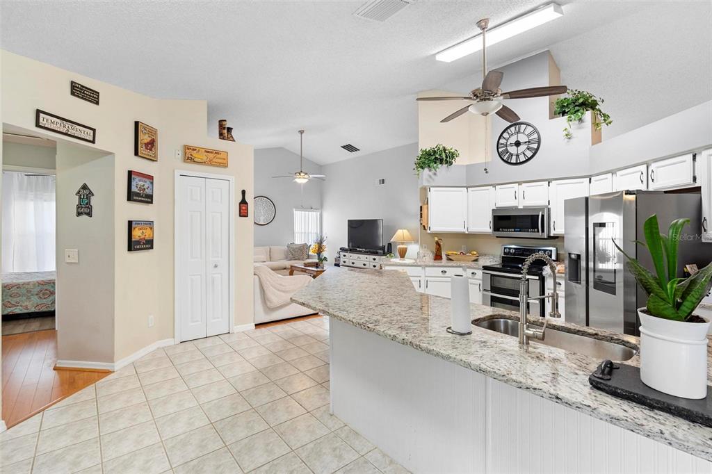 A kitchen with granite countertops and white cabinets opens into a living room area — 12512 TILLINGHAM COURT, ORLANDO, FL
