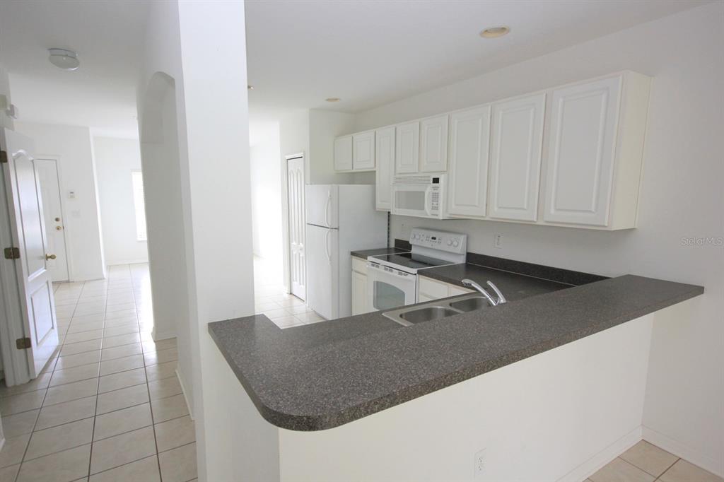 A kitchen with white cabinets, white appliances, and a dark gray countertop breakfast bar — 15643 STABLE RUN DRIVE, SPRING HILL, FL