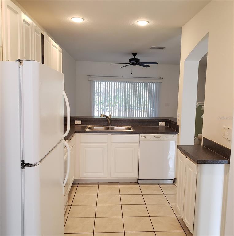 A kitchen features white cabinets, dark countertops, a white refrigerator, and a tiled floor — 15643 STABLE RUN DRIVE, SPRING HILL, FL
