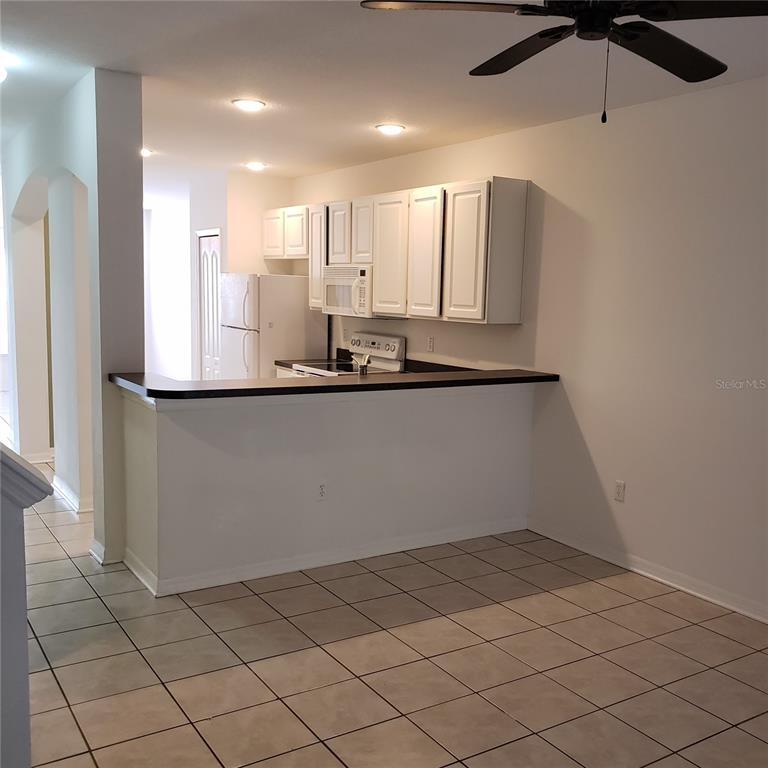 A kitchen features white cabinets, a black countertop, and tiled flooring in an open layout — 15643 STABLE RUN DRIVE, SPRING HILL, FL