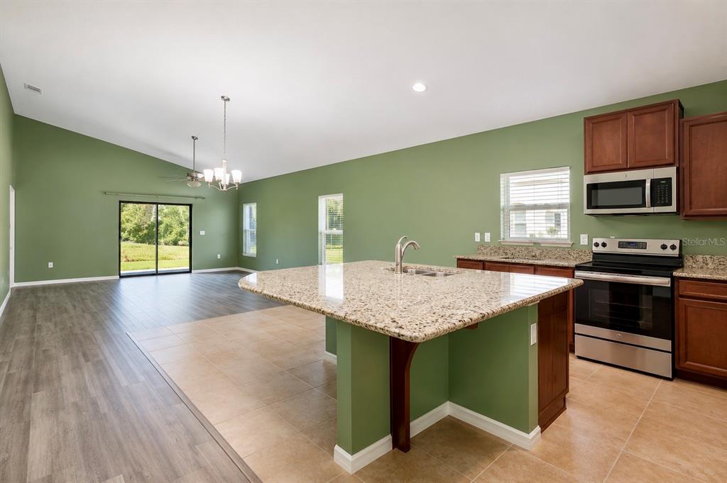 A kitchen with granite countertops and green walls opens to a living area with flooring — 5343 RADIANCE COURT, COCOA, FL