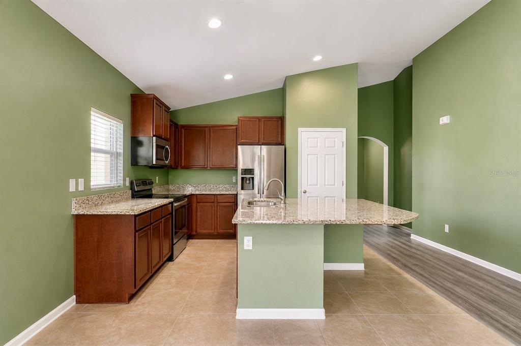 A kitchen features dark wood cabinets, granite countertops, tile flooring, and sage green walls — 5343 RADIANCE COURT, COCOA, FL