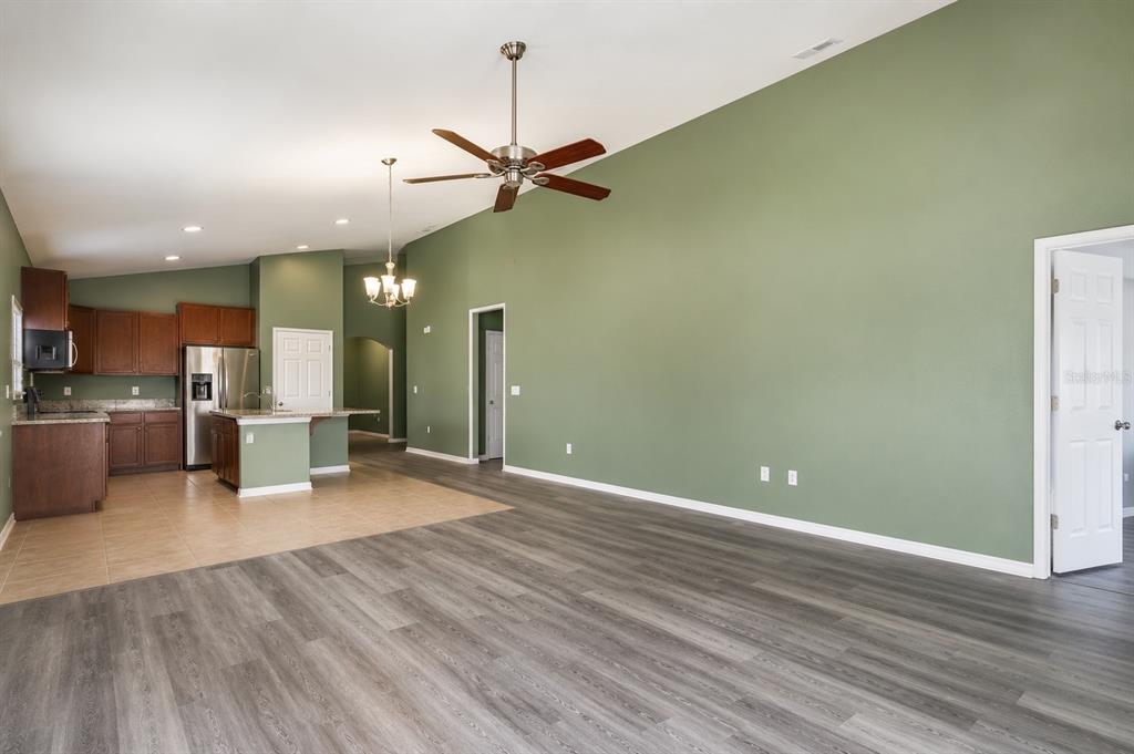An open-concept living room with gray wood-look flooring flows into a kitchen with brown cabinets — 5343 RADIANCE COURT, COCOA, FL