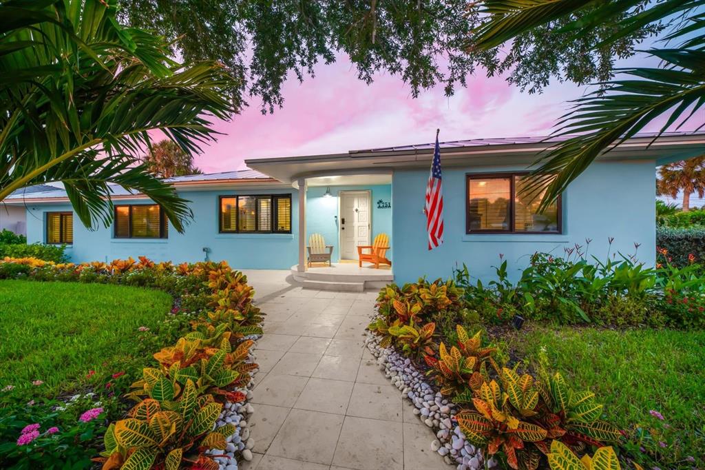 A light blue single-story house with a tiled walkway, colorful landscaping, and an American flag — 751 MANDALAY AVENUE, CLEARWATER BEACH, FL