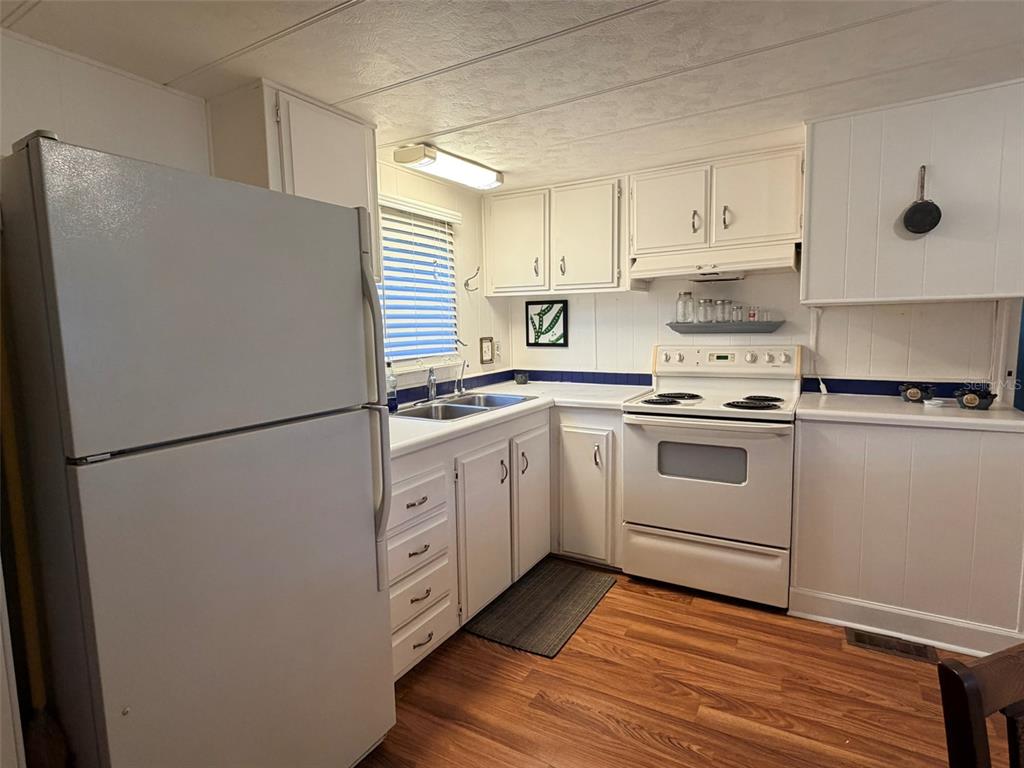 A kitchen features white cabinets, a white refrigerator, a white stove, and wood-look flooring — 2248 CA D ORO DRIVE, SARASOTA, FL