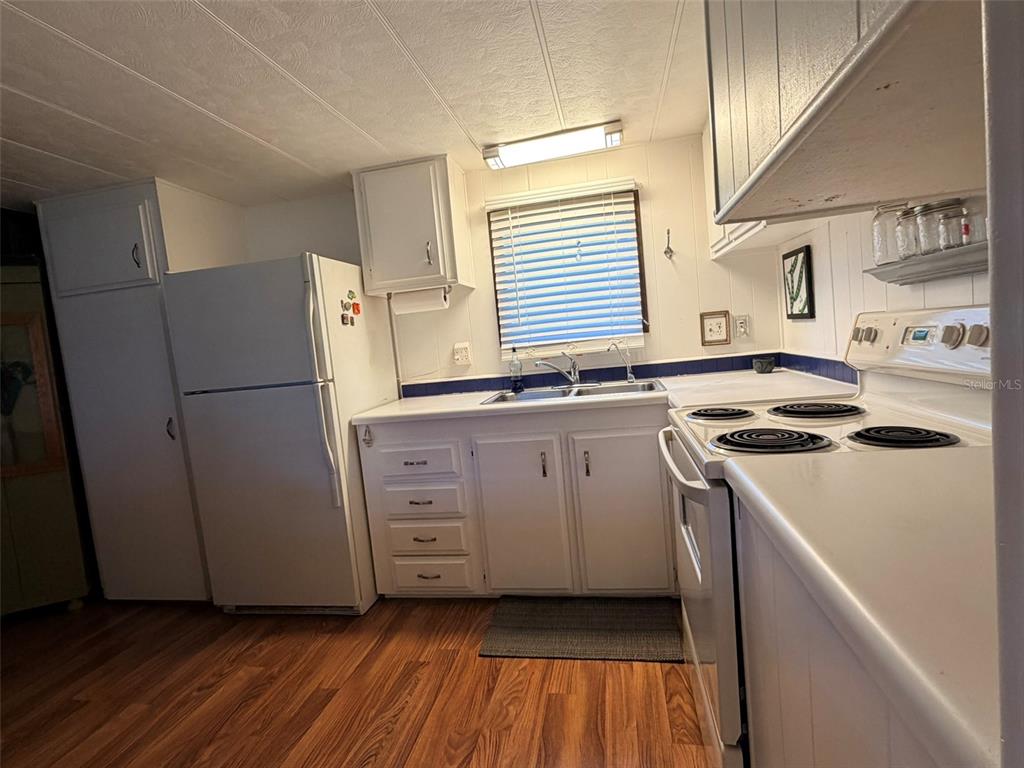 A kitchen features white cabinets, a white refrigerator, an electric stove, and wood-look flooring — 2248 CA D ORO DRIVE, SARASOTA, FL