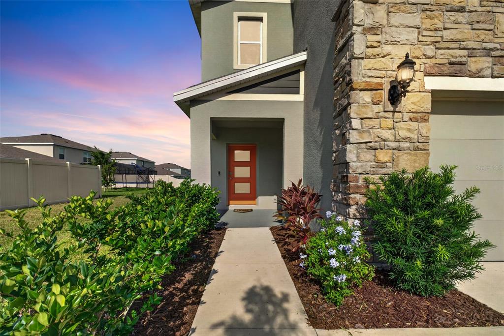 A concrete walkway leads to the orange front door of a house with stone siding — 9744 CRESCENT RAY DRIVE, WESLEY CHAPEL, FL