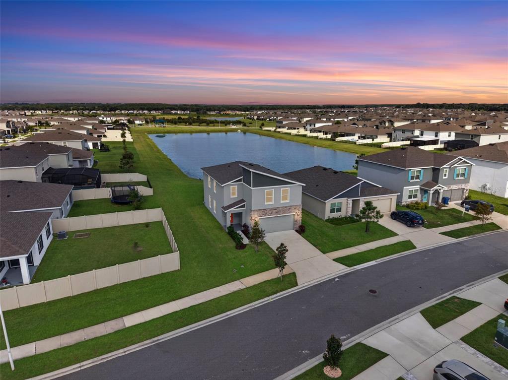 An aerial view shows a two-story suburban house with a gray exterior next to a pond — 9744 CRESCENT RAY DRIVE, WESLEY CHAPEL, FL