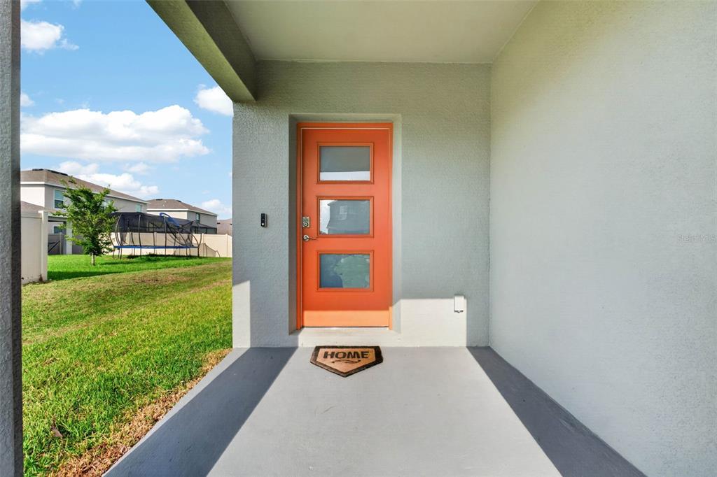 A covered entryway features a bright orange front door with three glass panels — 9744 CRESCENT RAY DRIVE, WESLEY CHAPEL, FL