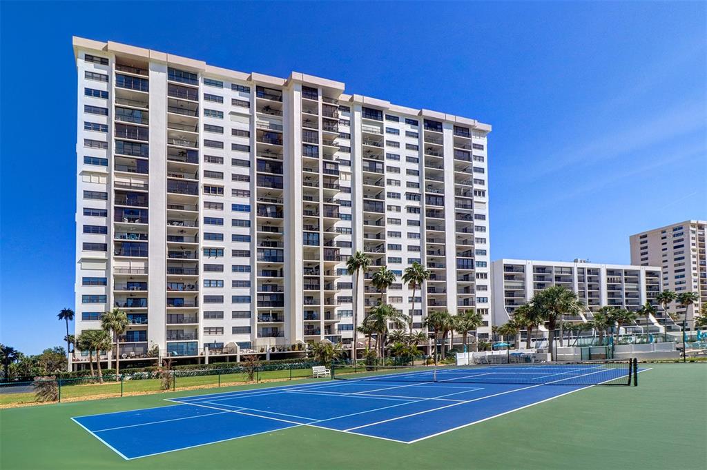 A blue tennis court sits in front of a large, multi-story residential apartment building — 1230 GULF BOULEVARD UNIT 404, CLEARWATER BEACH, FL
