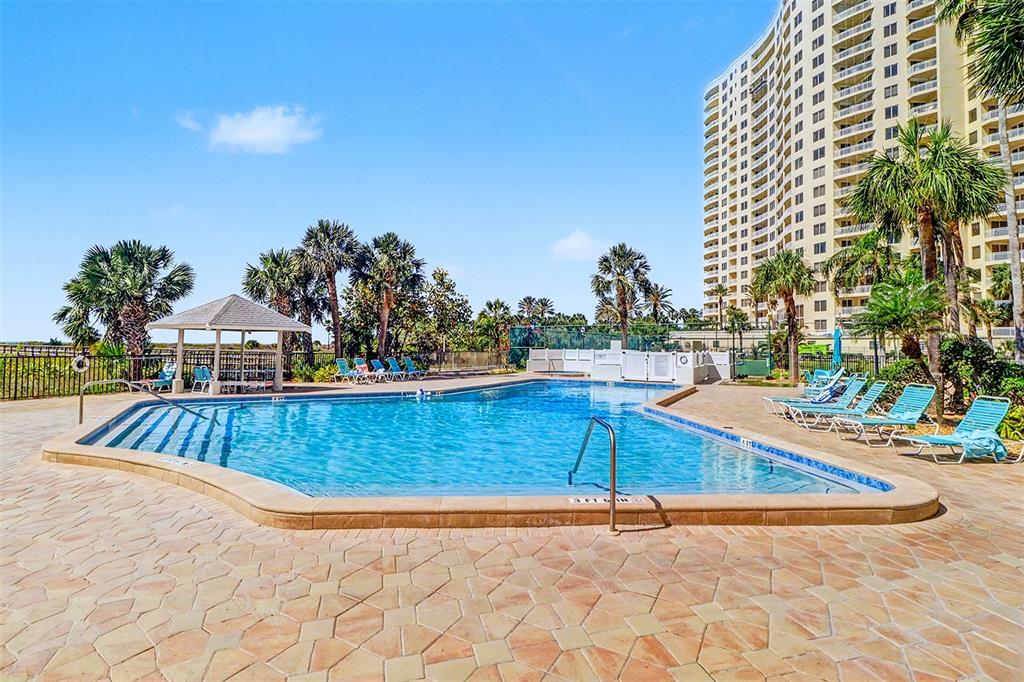 An outdoor swimming pool with lounge chairs and a gazebo sits beside a tall building — 1230 GULF BOULEVARD UNIT 404, CLEARWATER BEACH, FL