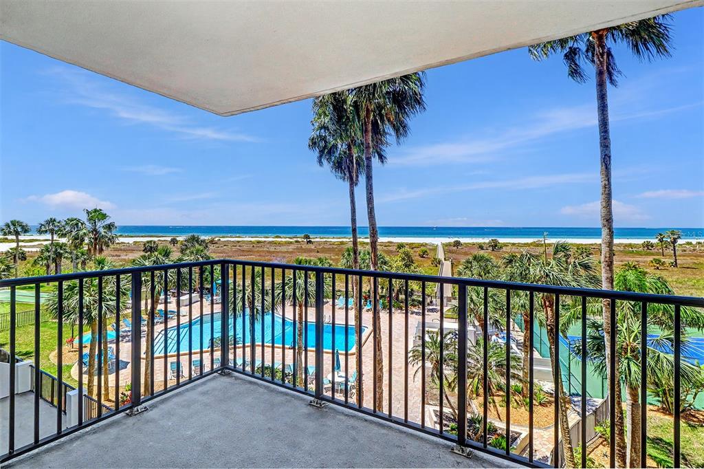 A balcony with a black metal railing overlooks a swimming pool, palm trees, and ocean — 1230 GULF BOULEVARD UNIT 404, CLEARWATER BEACH, FL