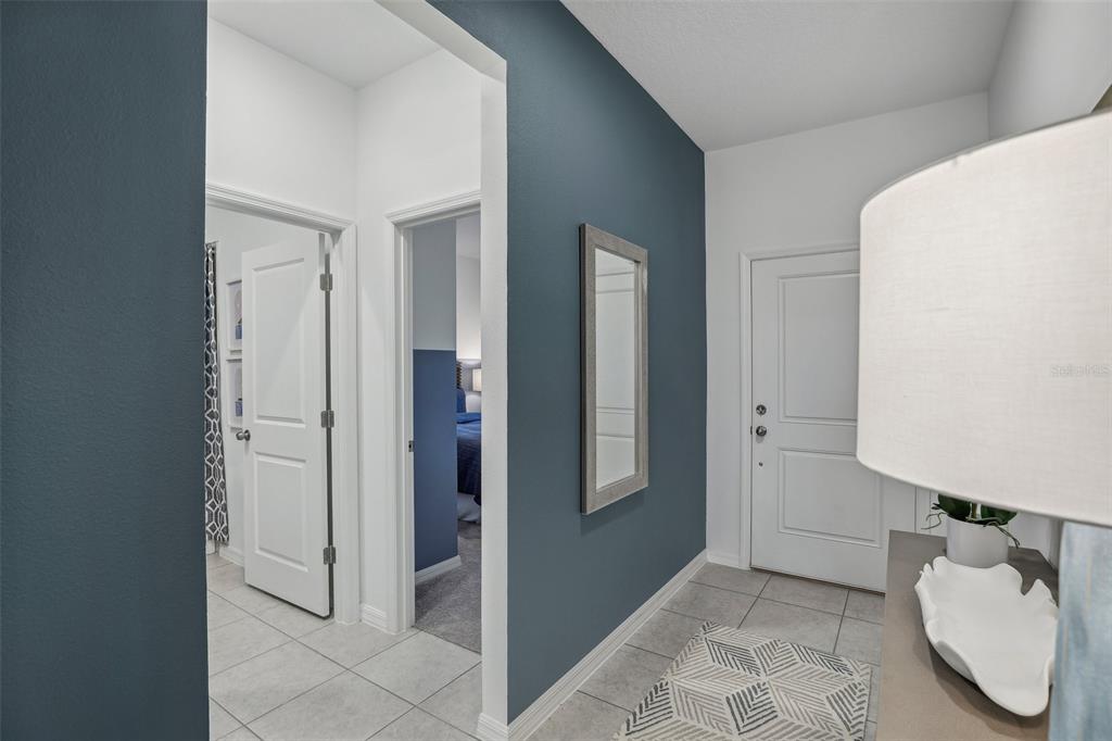 A hallway with blue accent walls, tile flooring, a mirror, and doors leading to other rooms — 9190 HARRIS HAWK DRIVE, LEESBURG, FL