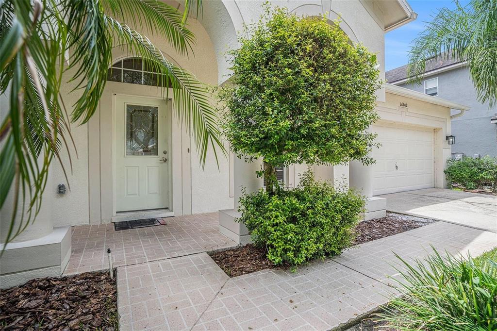 The exterior of a house features a white front door, a paved walkway, and landscaping — 16909 FALCONRIDGE ROAD, LITHIA, FL