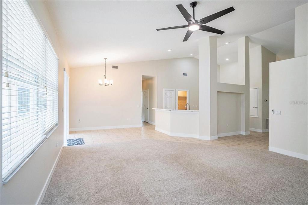 A living room with beige carpet, a ceiling fan, and an adjacent tiled dining area — 16909 FALCONRIDGE ROAD, LITHIA, FL